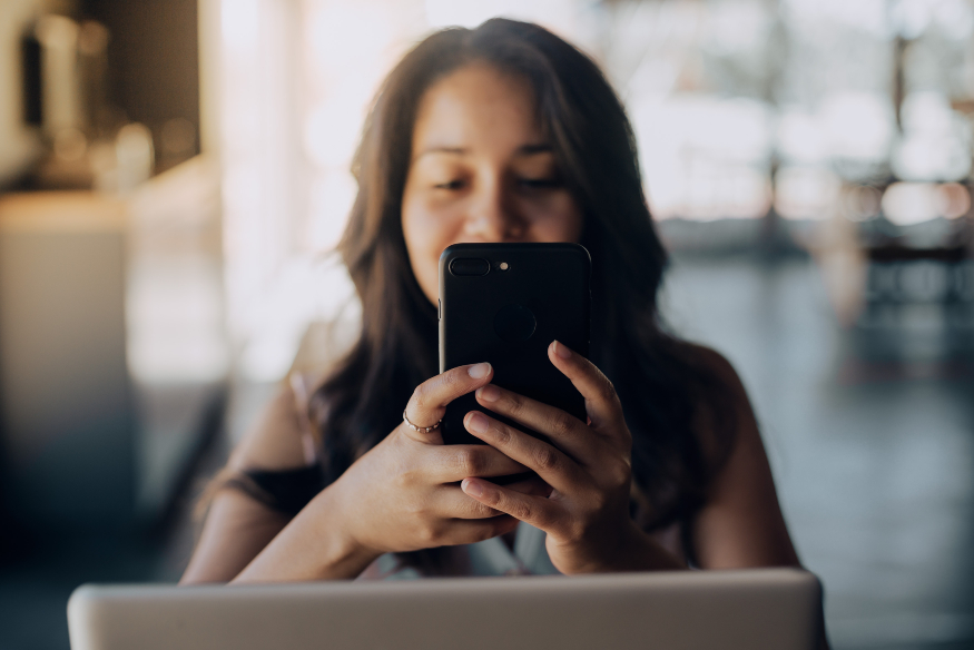 mujer sentada usando celular y sentada frente a una computadora investigando qué es la Cuenta 2.